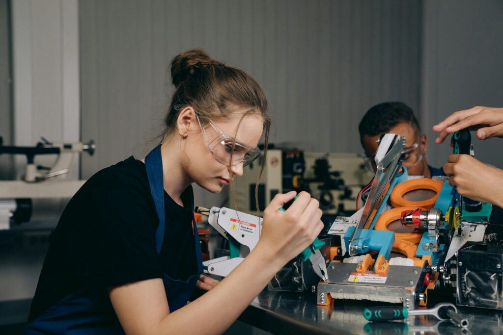 Female engineer in a workshop assembling robots with precision tools and safety gear.